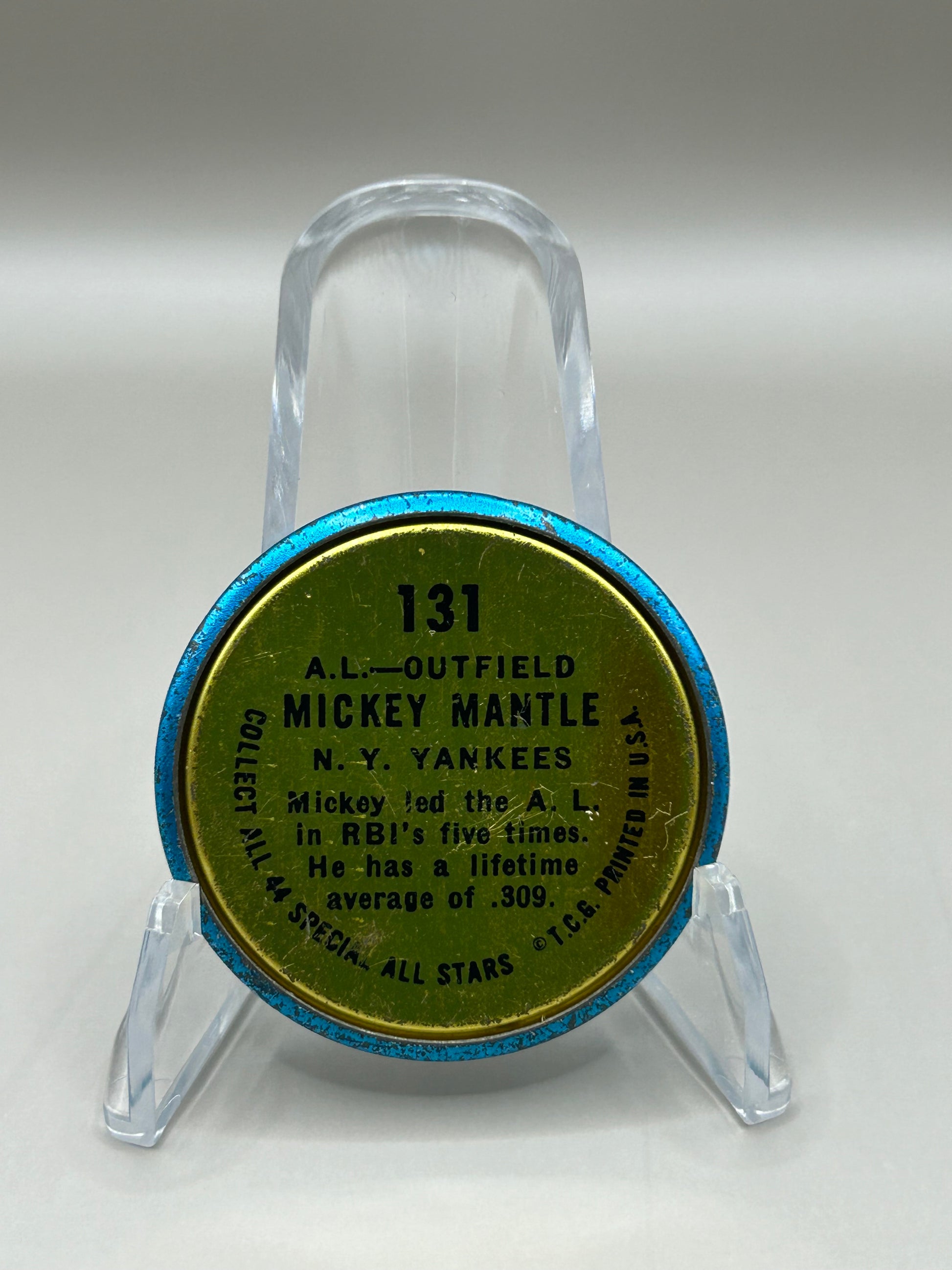 Back view of a 1964 Topps Mickey Mantle collectible coin with player details and stats, part of the '1964 All-Stars' series, displayed on a stand.